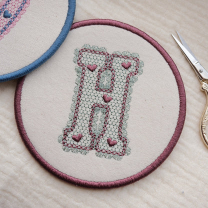 Round Embroidered Coaster with lace design initial, in Sage and Plum thread colourway, with gold scissors on the side