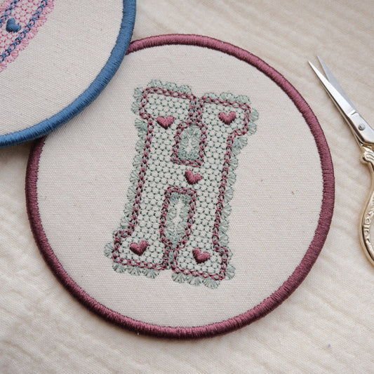 Round Embroidered Coaster with lace design initial, in Sage and Plum thread colourway, with gold scissors on the side