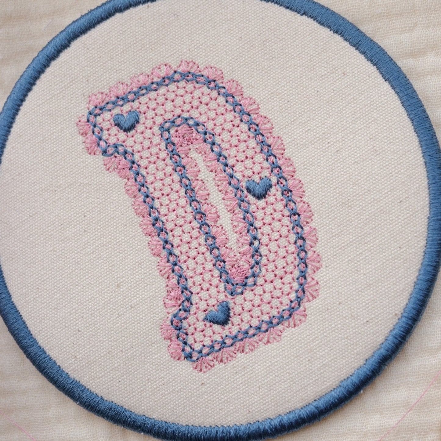 Close up of embroidered lace monogram letter D coaster with textured stitching and soft blue border detail