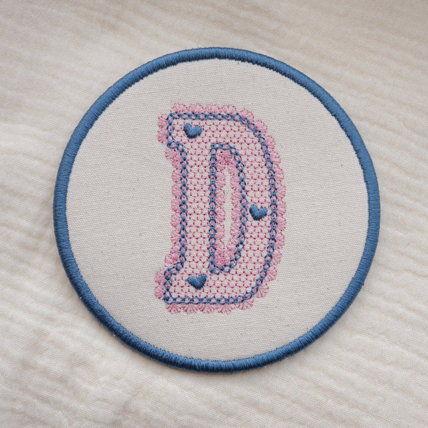 Custom embroidered initial coaster with lace inspired monogram design in pink and blue thread on neutral fabric
