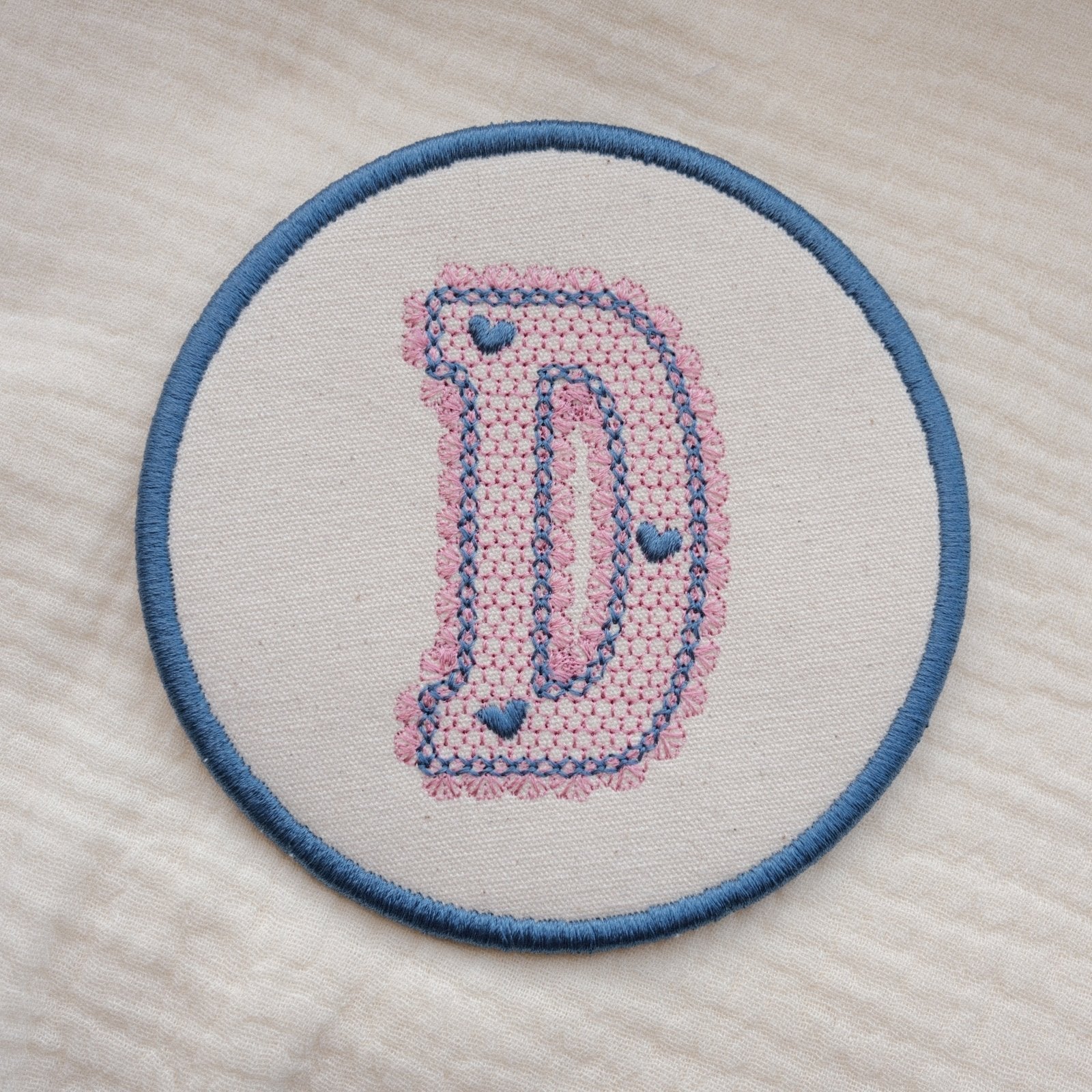 Custom embroidered initial coaster with lace inspired monogram design in pink and blue thread on neutral fabric