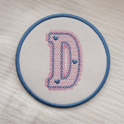 Custom embroidered initial coaster with lace inspired monogram design in pink and blue thread on neutral fabric
