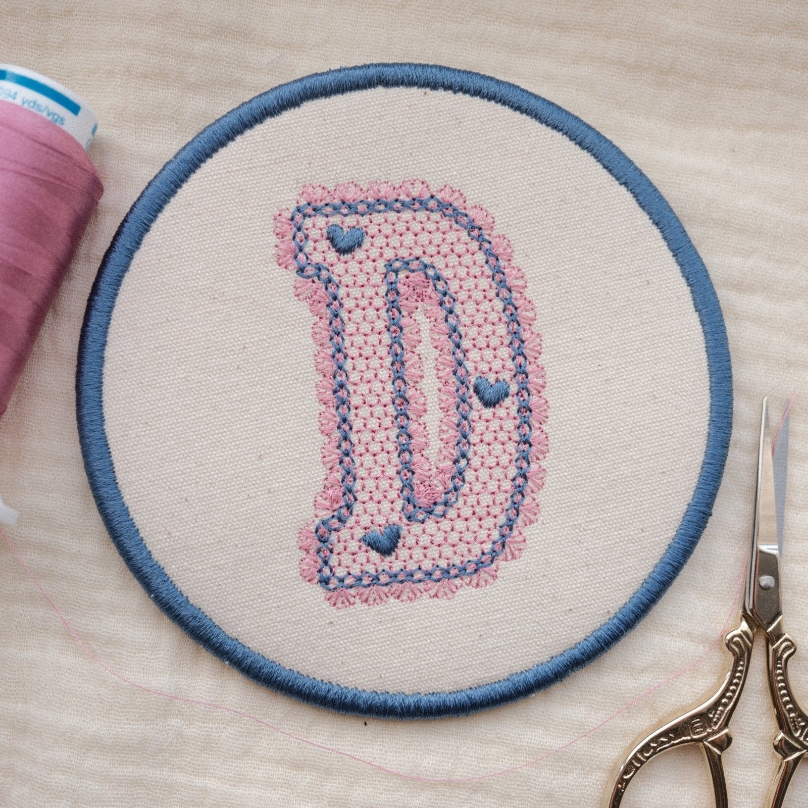 Handmade embroidered initial coaster featuring lace style letter D in pastel pink and blue thread colours