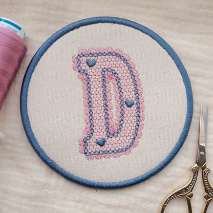Handmade embroidered initial coaster featuring lace style letter D in pastel pink and blue thread colours